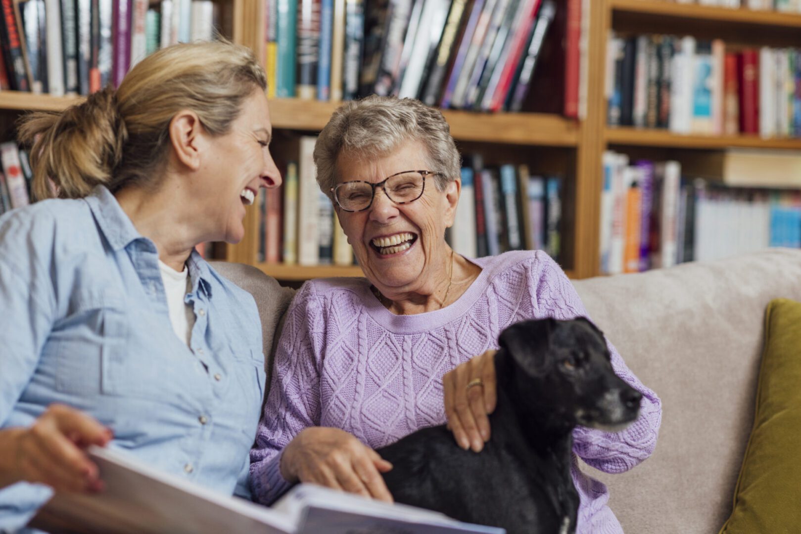 A mature woman sitting with her mother and pet dog on a sofa at home in Seghill, Northumberland. The senior woman is staying with her daughter for support and care as she has dementia and they are looking through a photo album together to aid her memory and strengthen their relationship.

Videos also available for similar scenario.